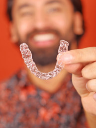 man with a perfect smile holding invisible aligners